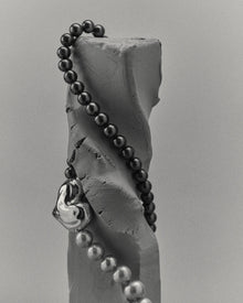 18K gold black pearl necklace with a 18K gold heart-shaped pendant on a clay sculpture
