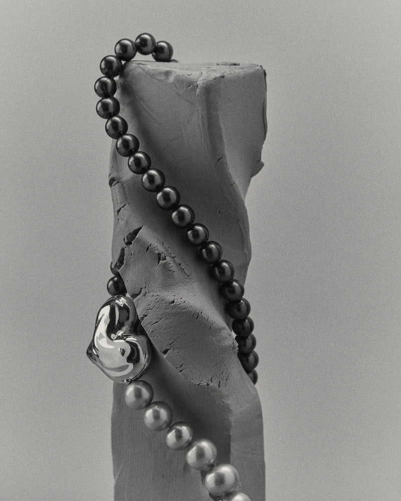 18K gold black pearl necklace with a 18K gold heart-shaped pendant on a clay sculpture