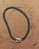 18K gold black pearl necklace with a 18K gold pomegranate-shaped pendant on a sand