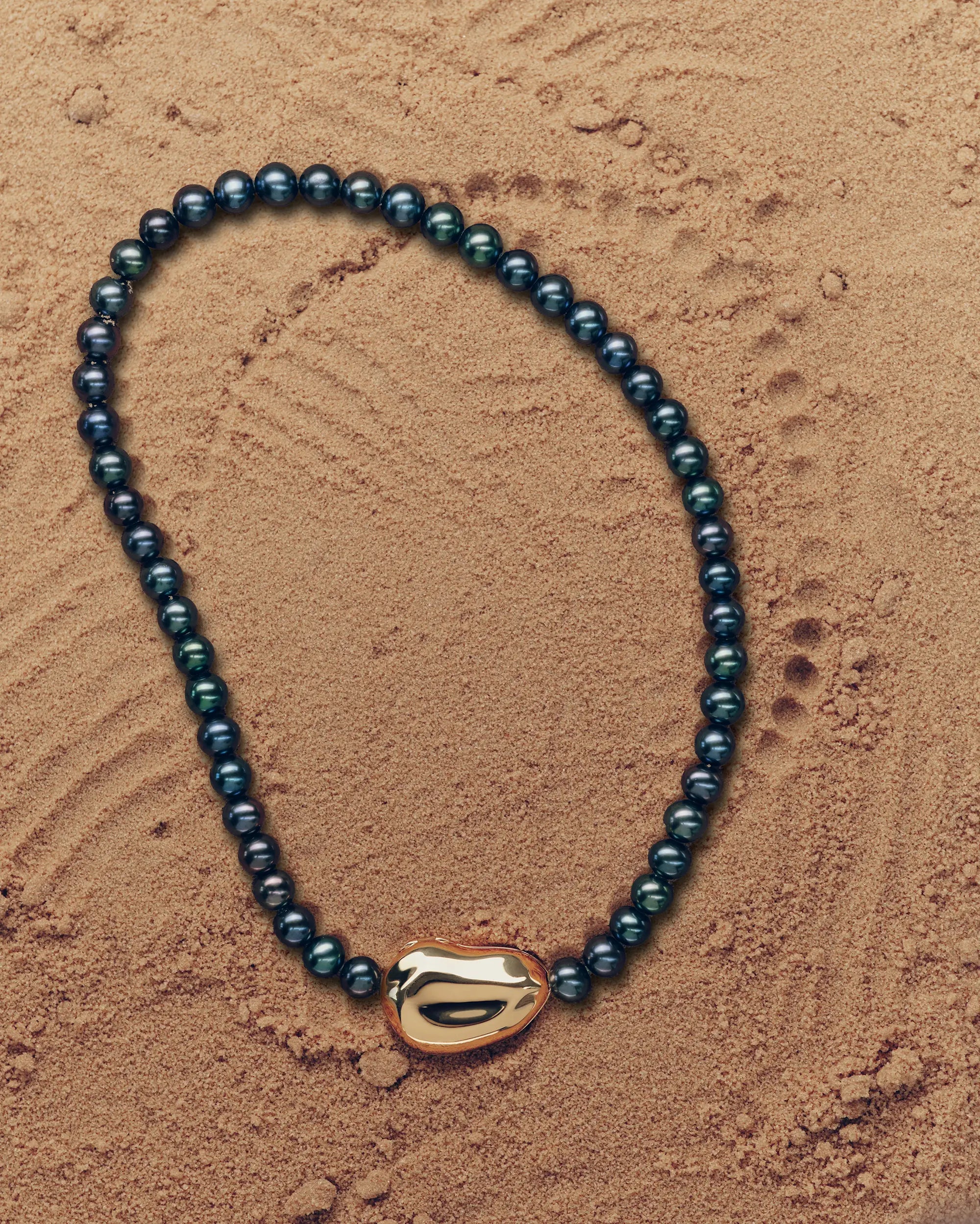 18K gold black pearl necklace with a 18K gold pomegranate-shaped pendant on a sand