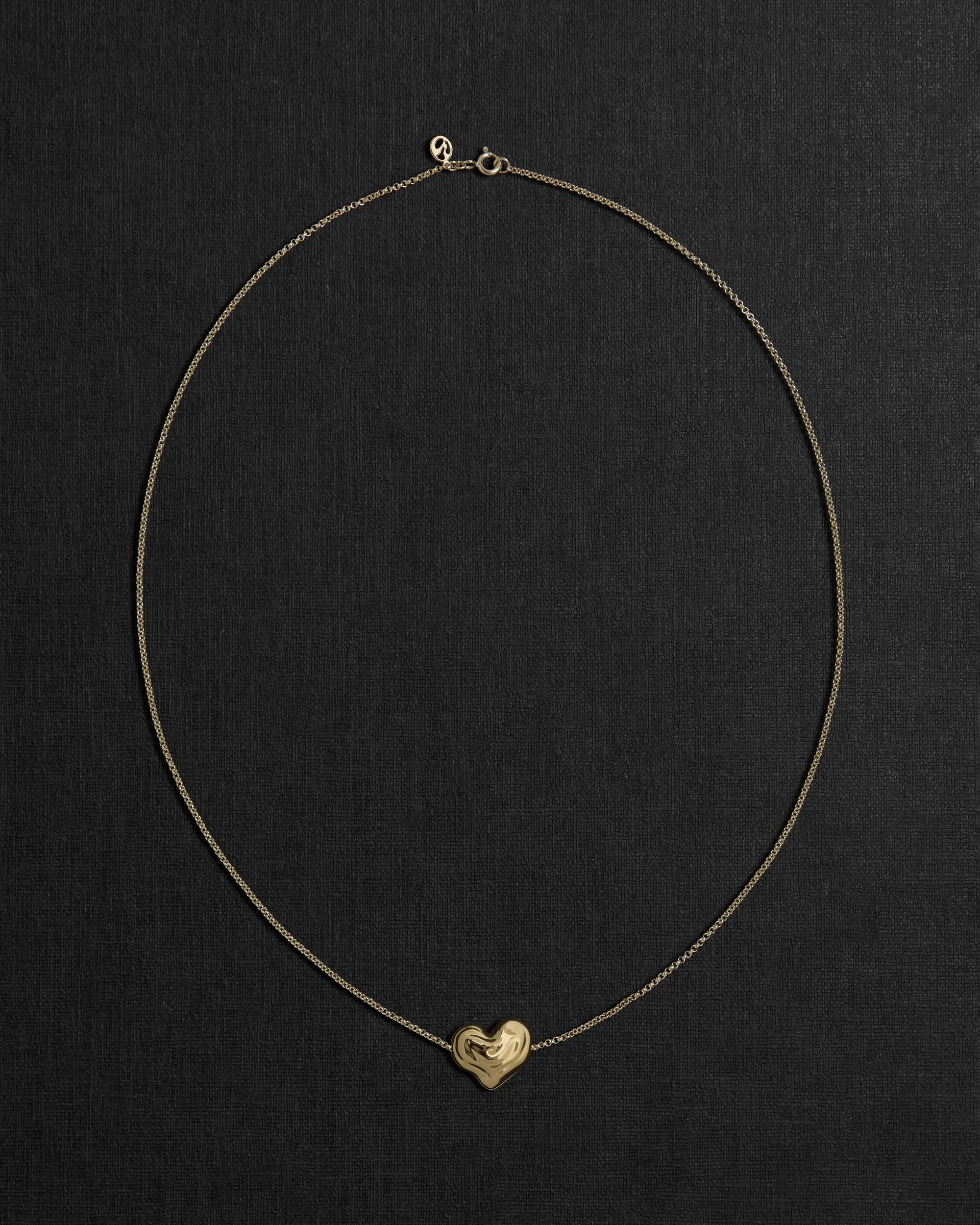 18K gold rollo chain necklace with a heart-shaped pendant on a black background