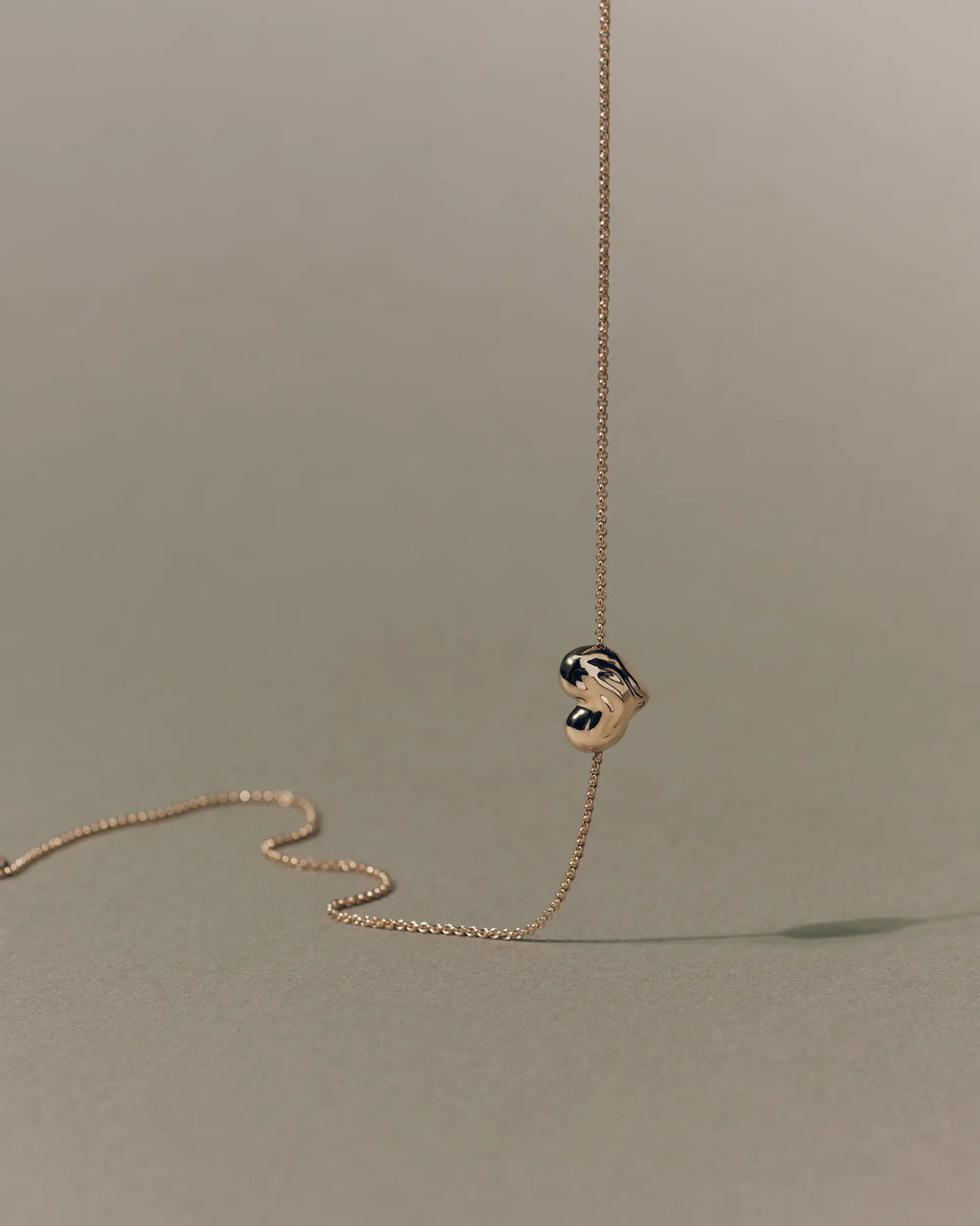 18K gold rollo chain necklace with a heart-shaped pendant on a beige background