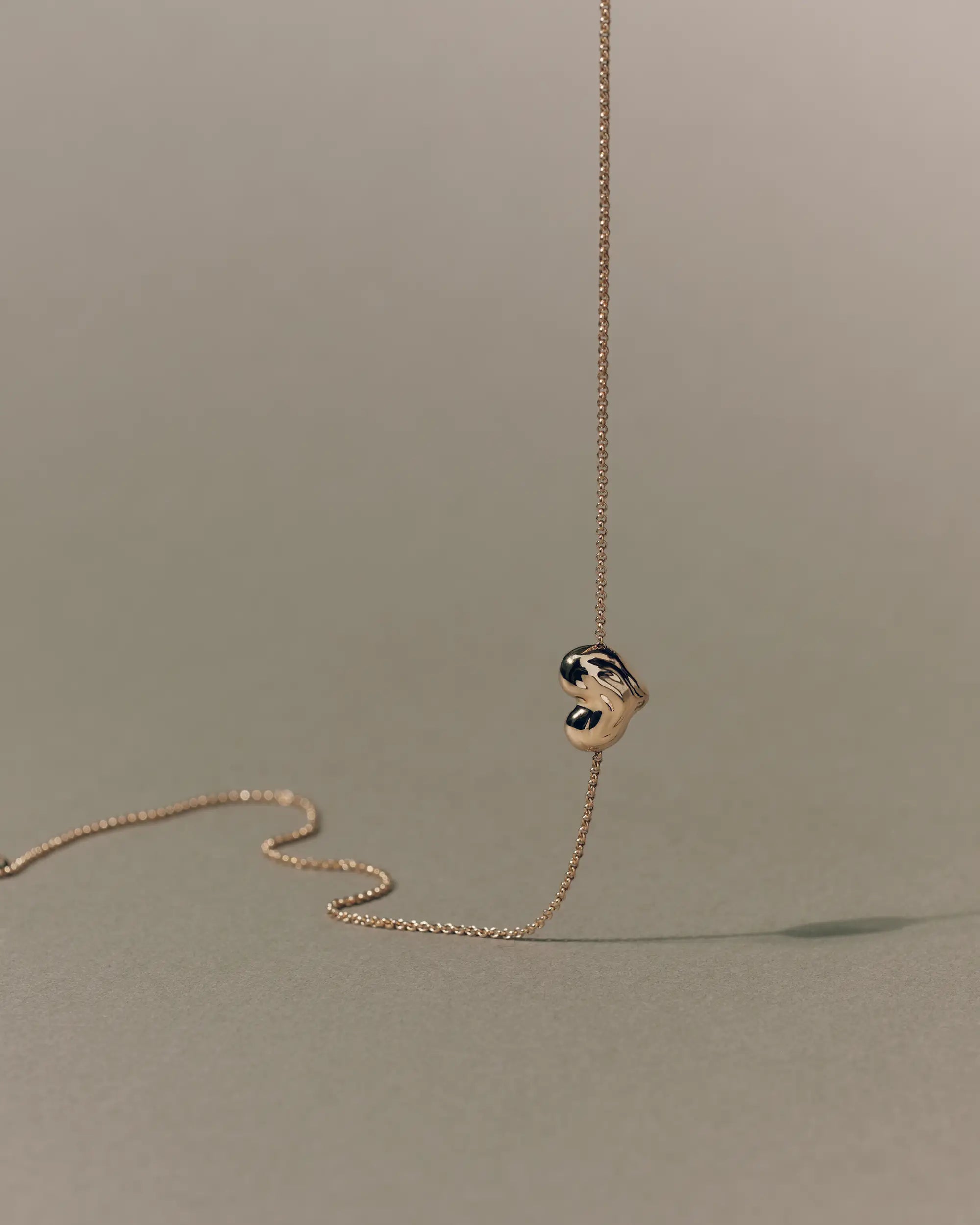 18K gold rollo chain necklace with a heart-shaped pendant on a beige background