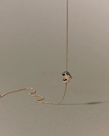18K gold rollo chain necklace with a heart-shaped pendant on a beige background