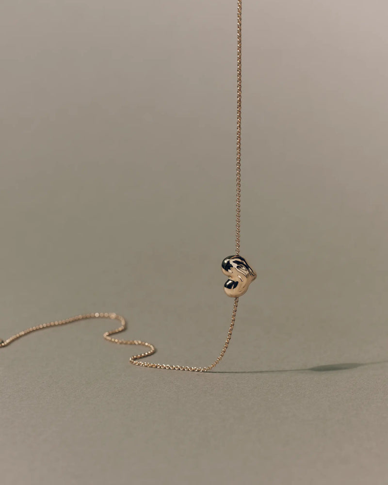 18K gold rollo chain necklace with a heart-shaped pendant on a beige background