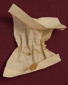 18K gold rollo chain necklace with a heart-shaped pendant on crumpled beige tissue paper against a pink linen background