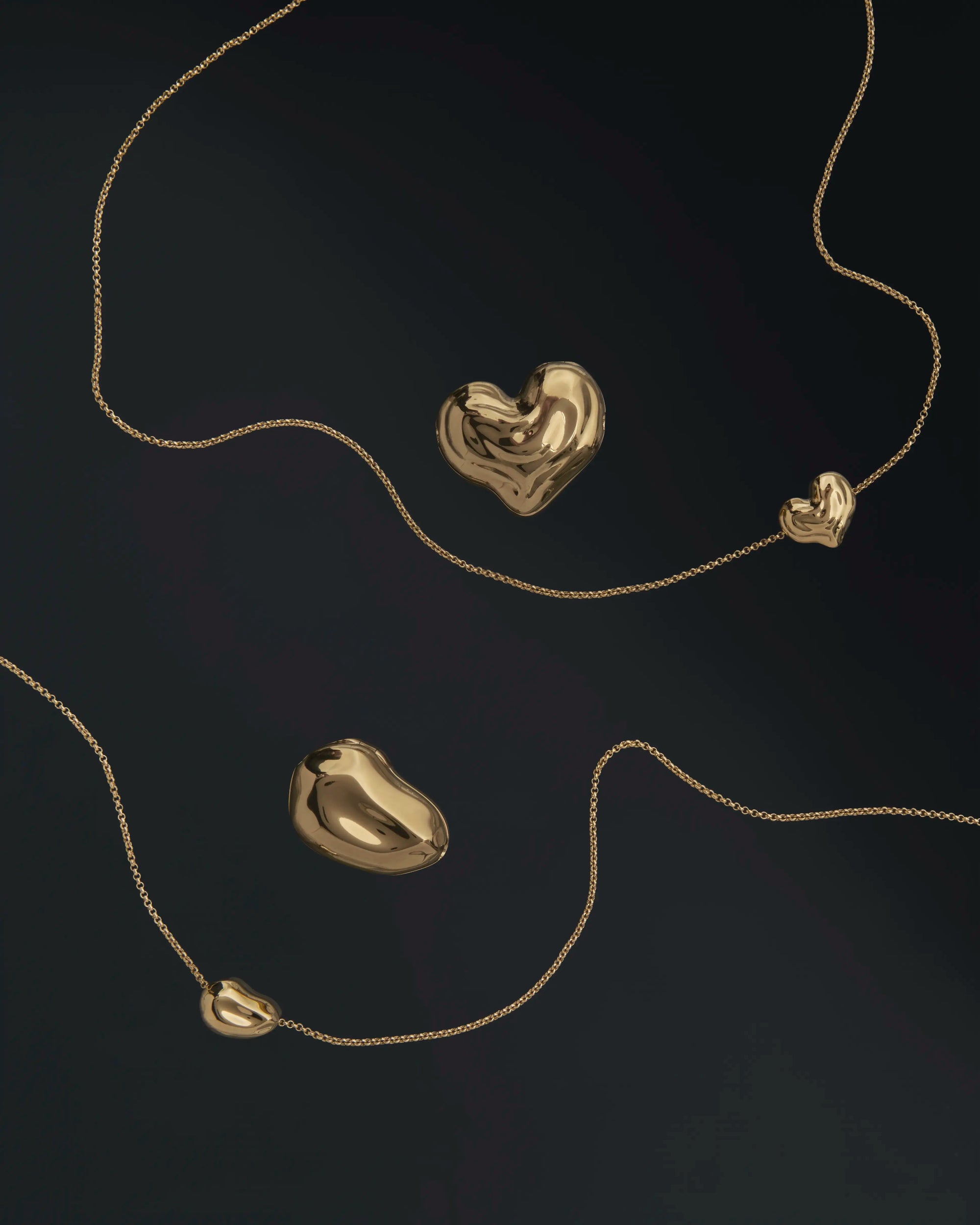 18K gold rollo chain necklaces with a heart-shaped and pomegranate-shaped pendants on a black background