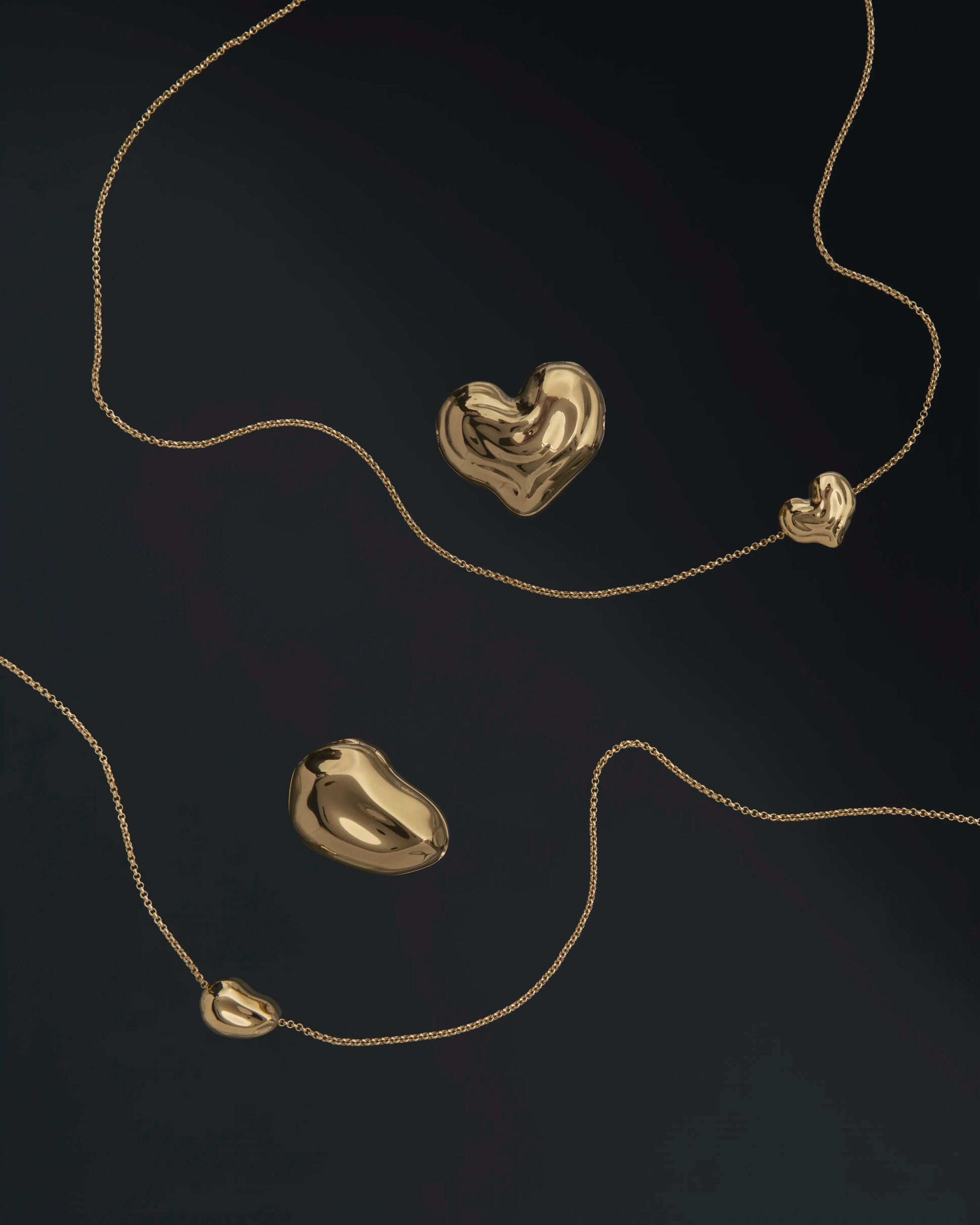 18K gold rollo chain necklaces with a heart-shaped and pomegranate-shaped pendants on a black background