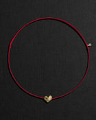 Red cord necklace with a 18K gold heart-shaped pendant on a black background