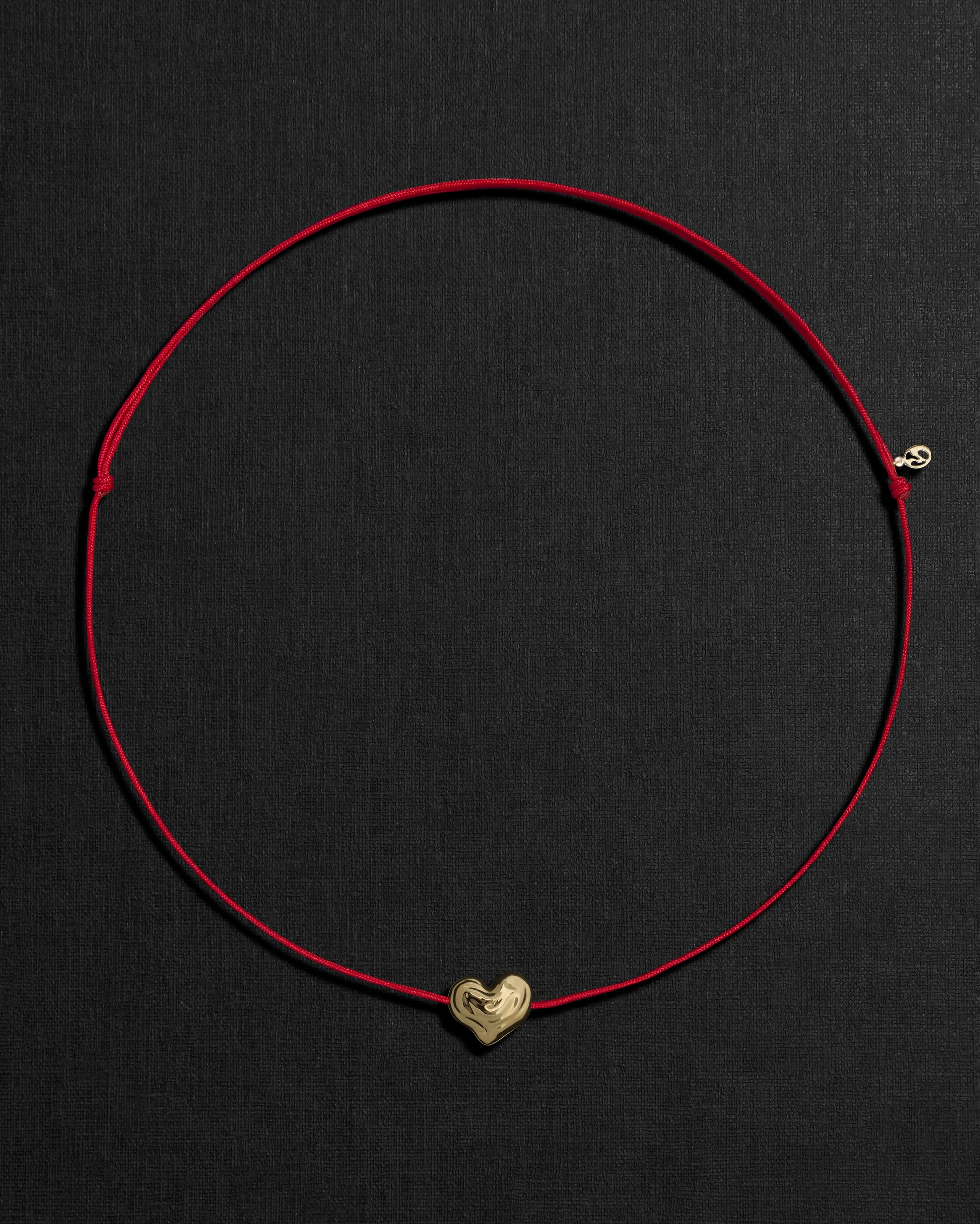 Red cord necklace with a 18K gold heart-shaped pendant on a black background