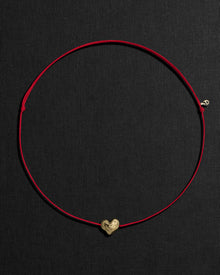 Red cord necklace with a 18K gold heart-shaped pendant on a black background