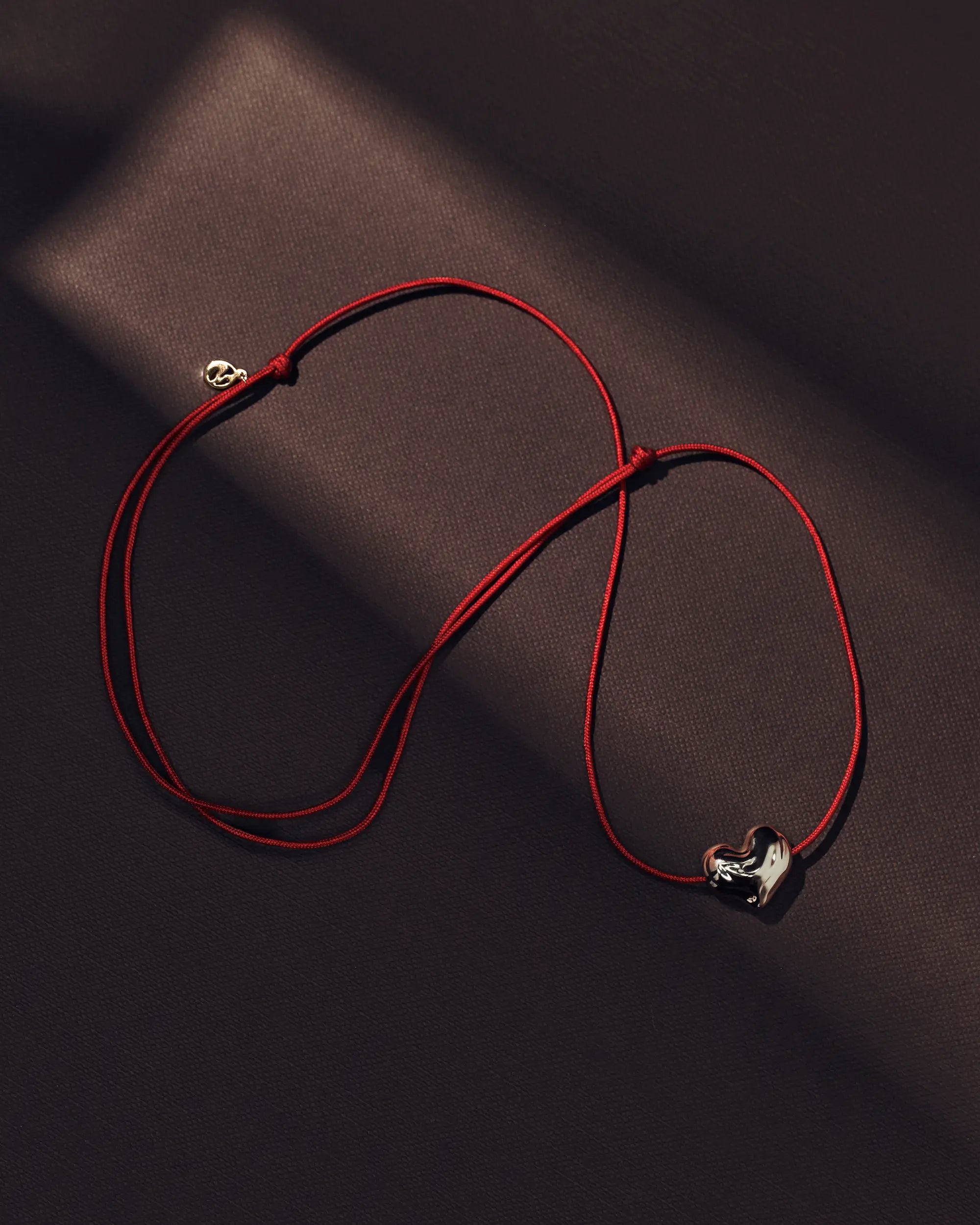Red cord necklace with a 18K gold heart-shaped pendant on a brown background
