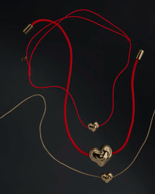 Red cord and rollo chain necklaces with 18K gold heart-shaped pendants on a black background