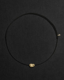 Black cord necklace with a 18K gold pomegranate-shaped pendant on a black background