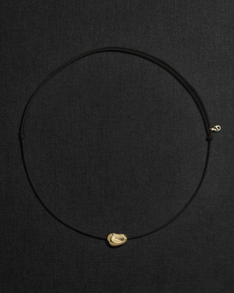 Black cord necklace with a 18K gold pomegranate-shaped pendant on a black background