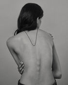 Model wearing black cord necklace with a 18K gold pomegranate-shaped pendant on a grey background