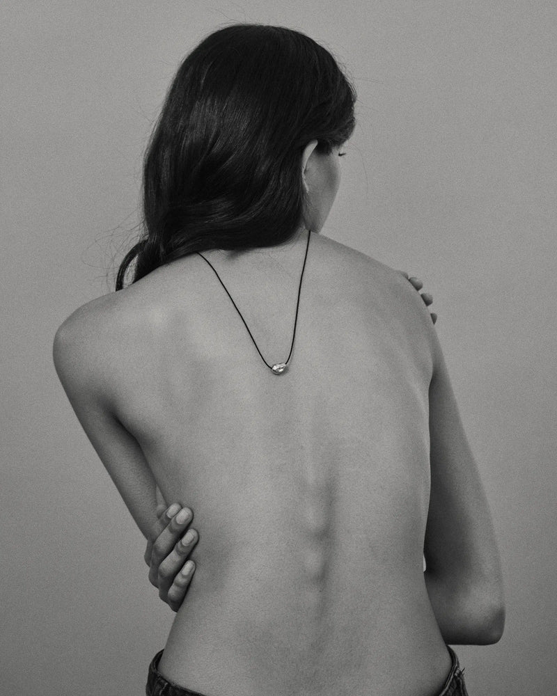 Model wearing black cord necklace with a 18K gold pomegranate-shaped pendant on a grey background