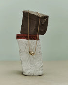 18K gold rollo chain necklace with a pomegranate-shaped pendant on a clay sculpture