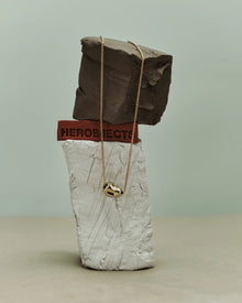18K gold rollo chain necklace with a pomegranate-shaped pendant on a clay sculpture