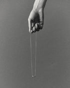 Hand holding a 18K gold rollo chain necklace with a pomegranate-shaped pendant on a grey background