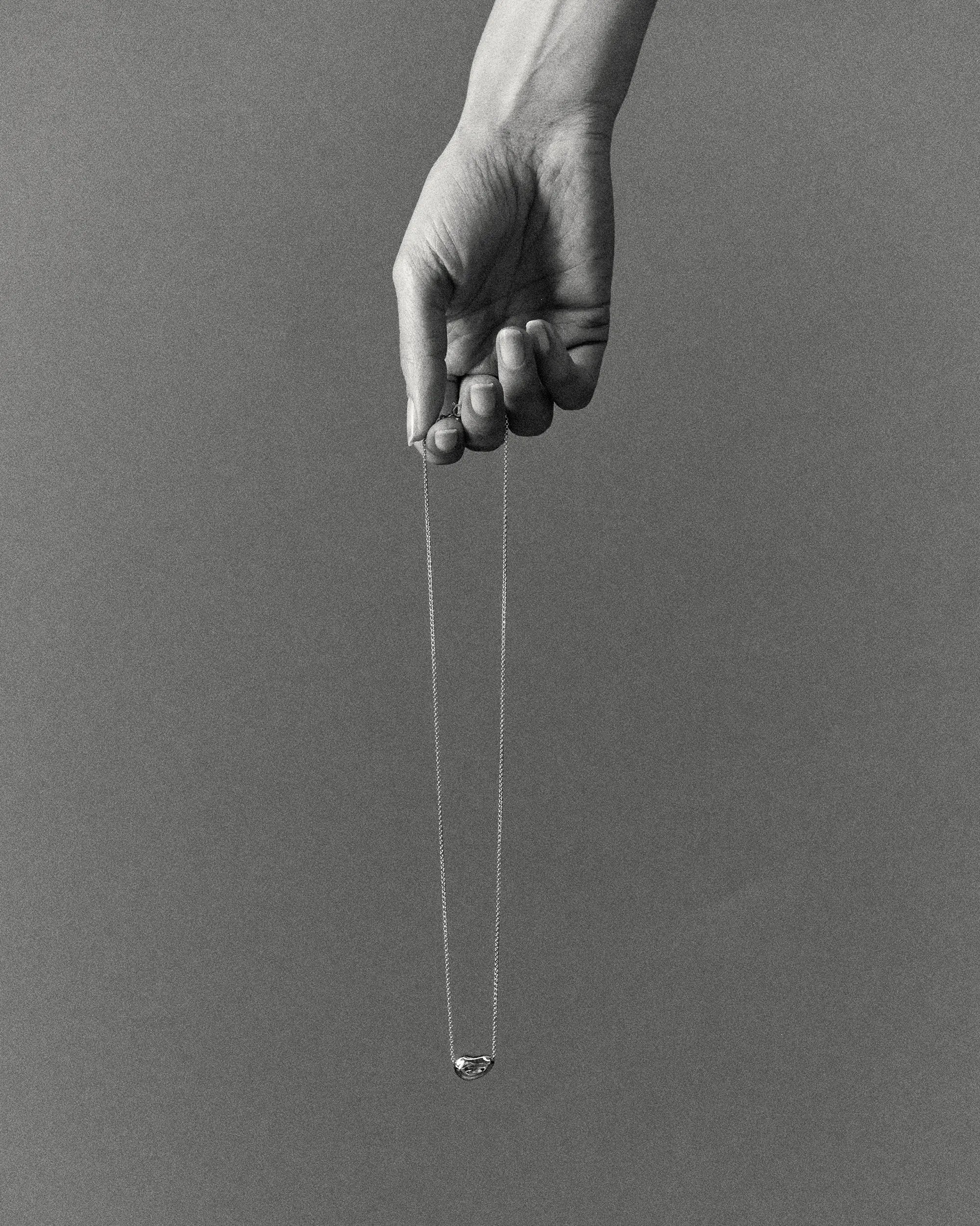 Hand holding a 18K gold rollo chain necklace with a pomegranate-shaped pendant on a grey background