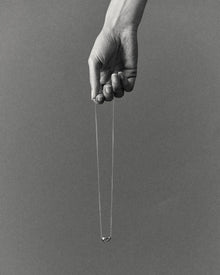 Hand holding a 18K gold rollo chain necklace with a pomegranate-shaped pendant on a grey background