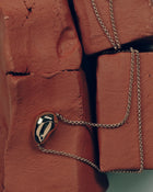 18K gold rollo chain necklace with a pomegranate-shaped pendant on a clay block