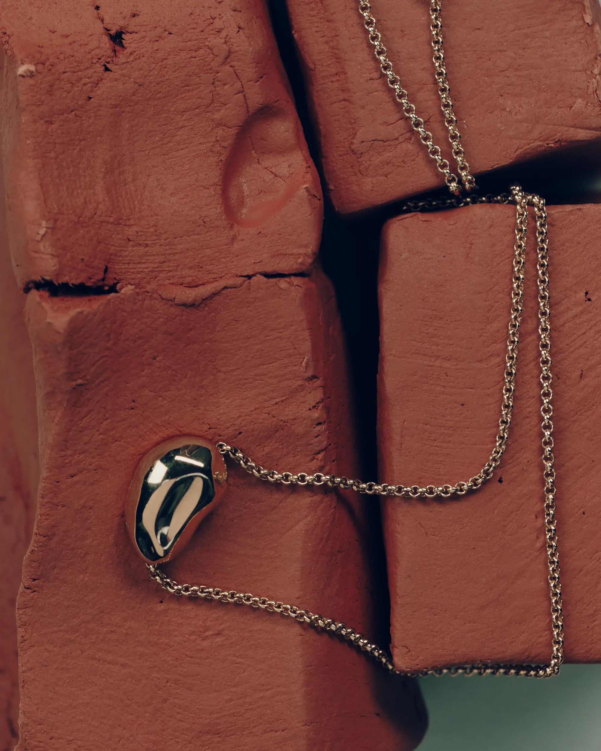 18K gold rollo chain necklace with a pomegranate-shaped pendant on a clay block
