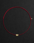 Red cord necklace with a 18K gold pomegranate-shaped pendant on a black background