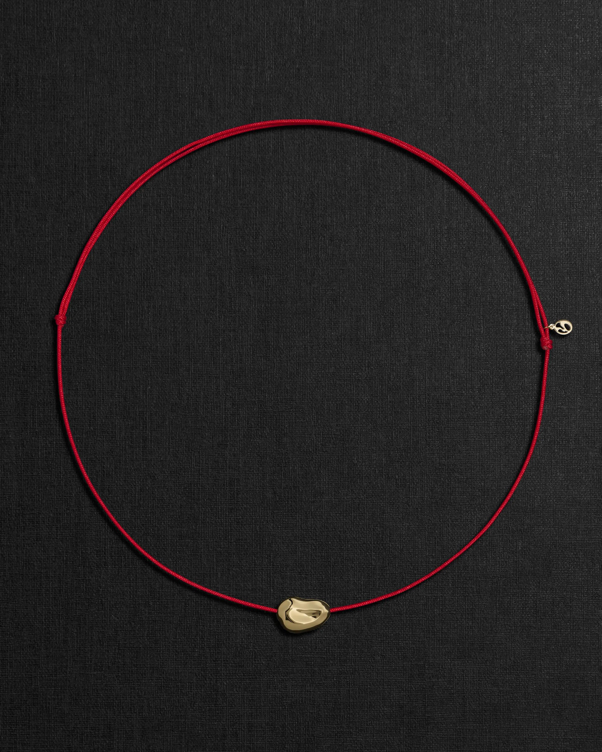 Red cord necklace with a 18K gold pomegranate-shaped pendant on a black background