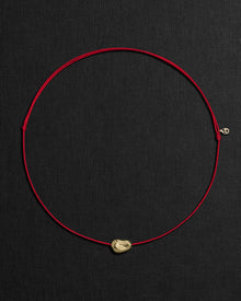 Red cord necklace with a 18K gold pomegranate-shaped pendant on a black background