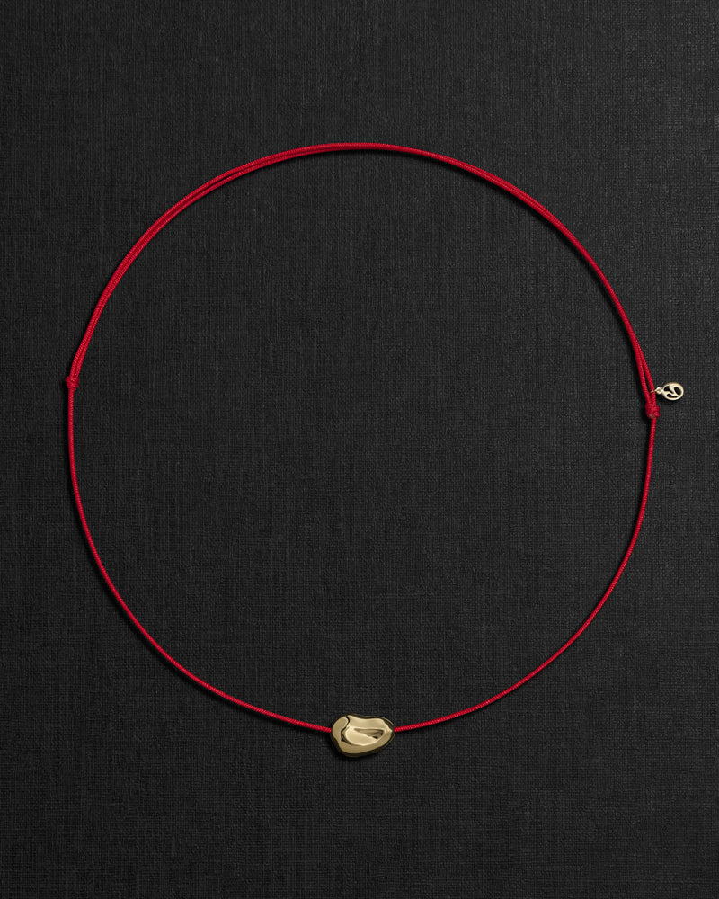 Red cord necklace with a 18K gold pomegranate-shaped pendant on a black background