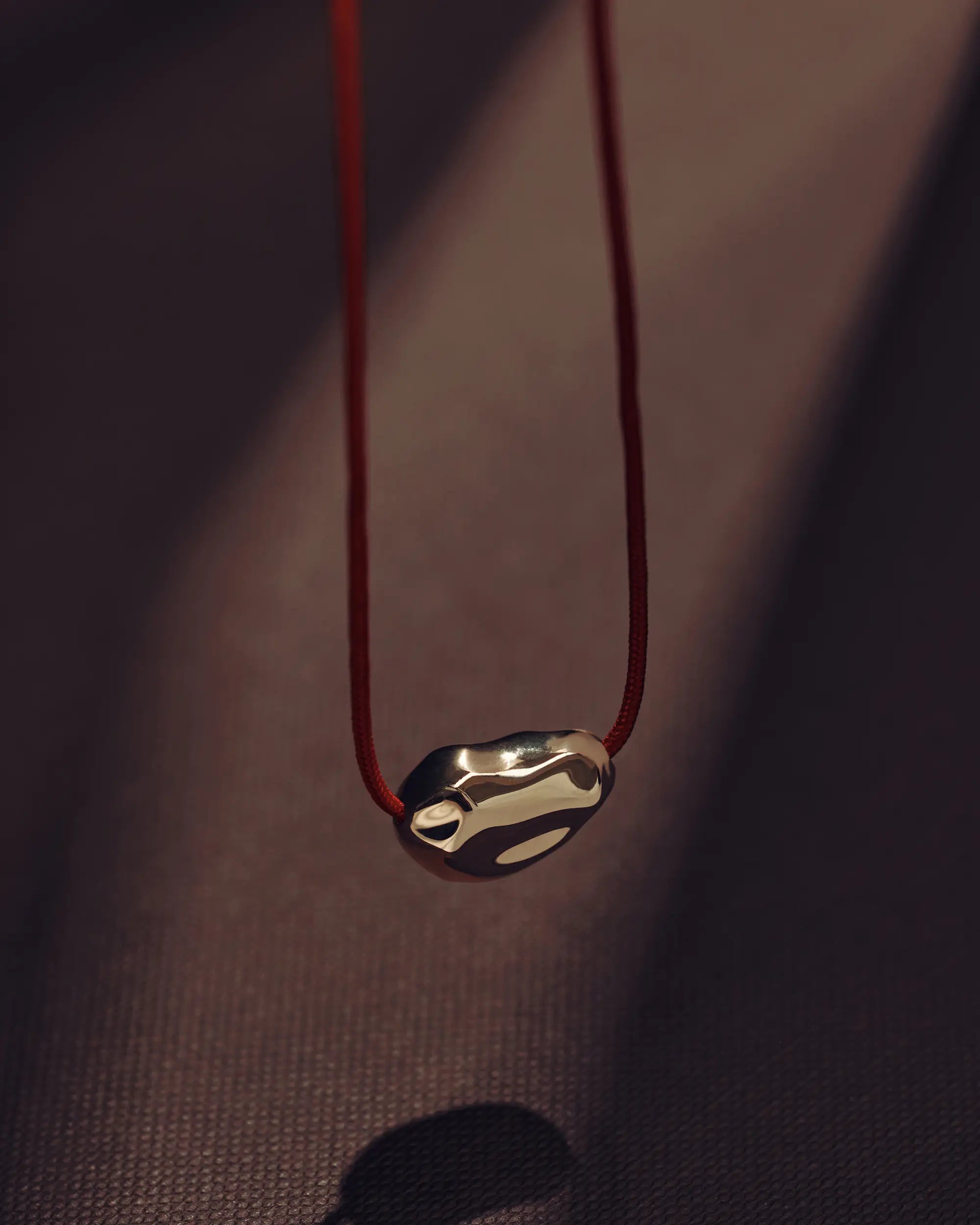 Red cord necklace with a 18K gold pomegranate-shaped pendant on a brown background