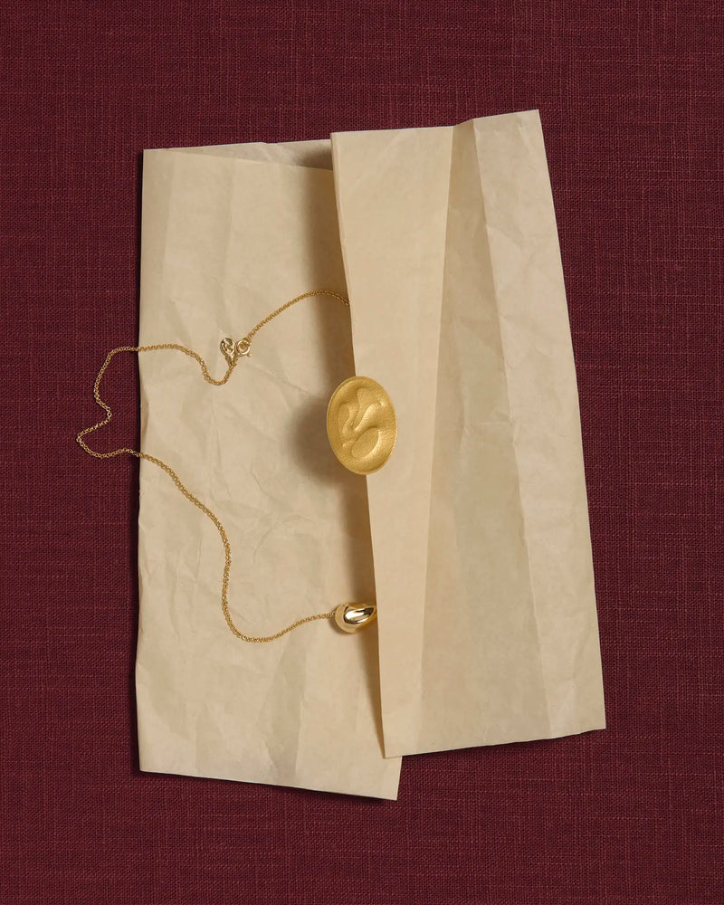 18K gold rollo chain necklace with a pomegranate-shaped pendant on a tissue paper and pink linen background