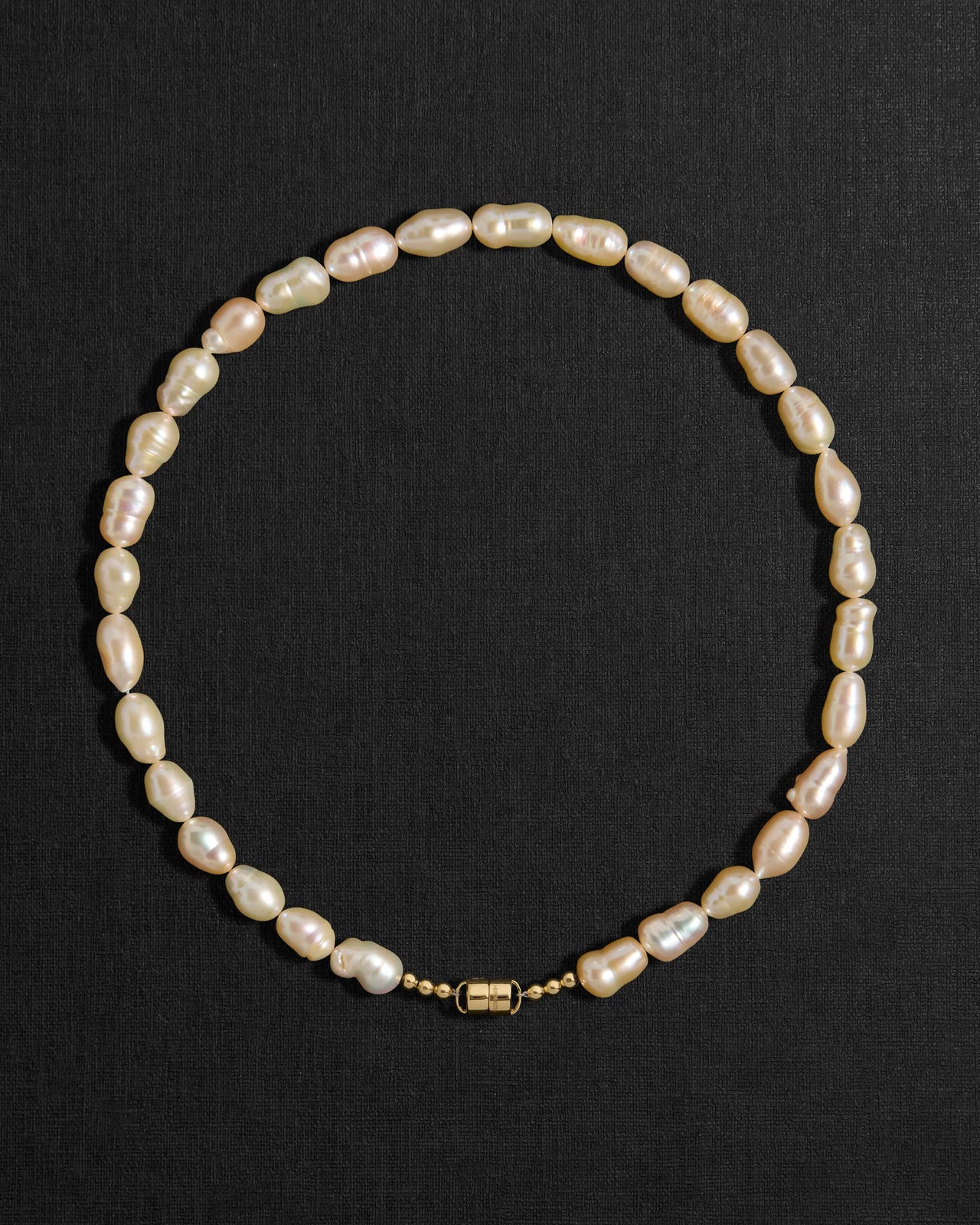 Peach pearl necklace with a 18K gold clasp on a black background