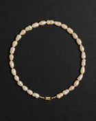 Peach pearl necklace with a 18K gold clasp on a black background