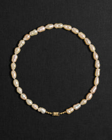 Peach pearl necklace with a 18K gold clasp on a black background