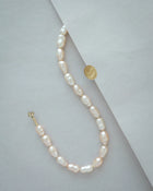 A 18K gold peach pearl necklace with irregular, teardrop-shaped pearls, displayed on a light grey background with a gold sticker prop.