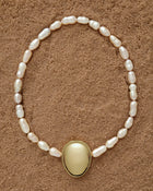 18K Gold Hero Pebble pendant and 18K Gold Freshwater pearl in Peach on a sand