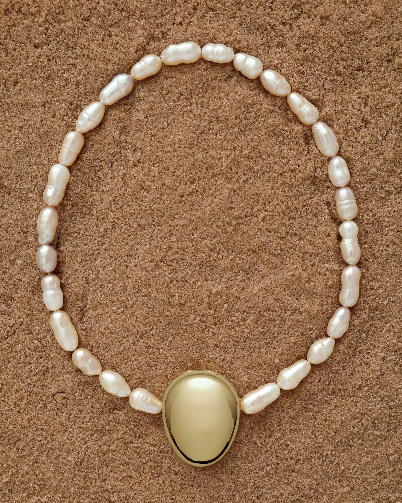 18K Gold Hero Pebble pendant and 18K Gold Freshwater pearl in Peach on a sand
