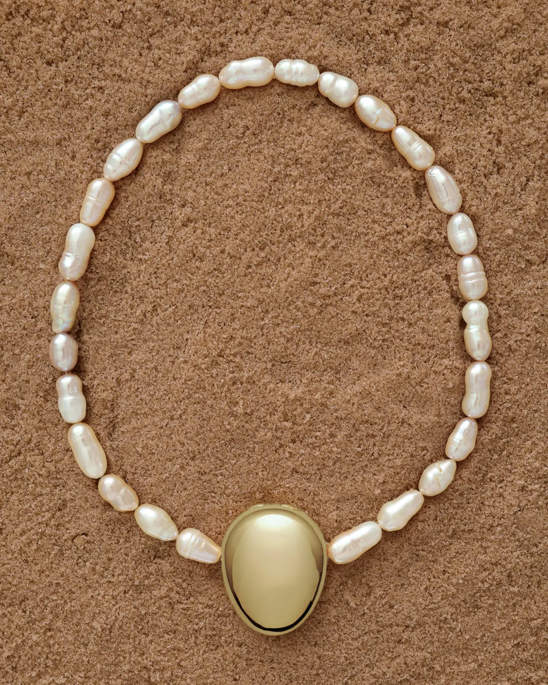 18K Gold Hero Pebble pendant and 18K Gold Freshwater pearl in Peach on a sand