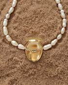 Opened 18K Gold Hero Pebble pendant and 18K Gold Freshwater pearl in Peach on a sand