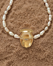 Opened 18K Gold Hero Pebble pendant and 18K Gold Freshwater pearl in Peach on a sand