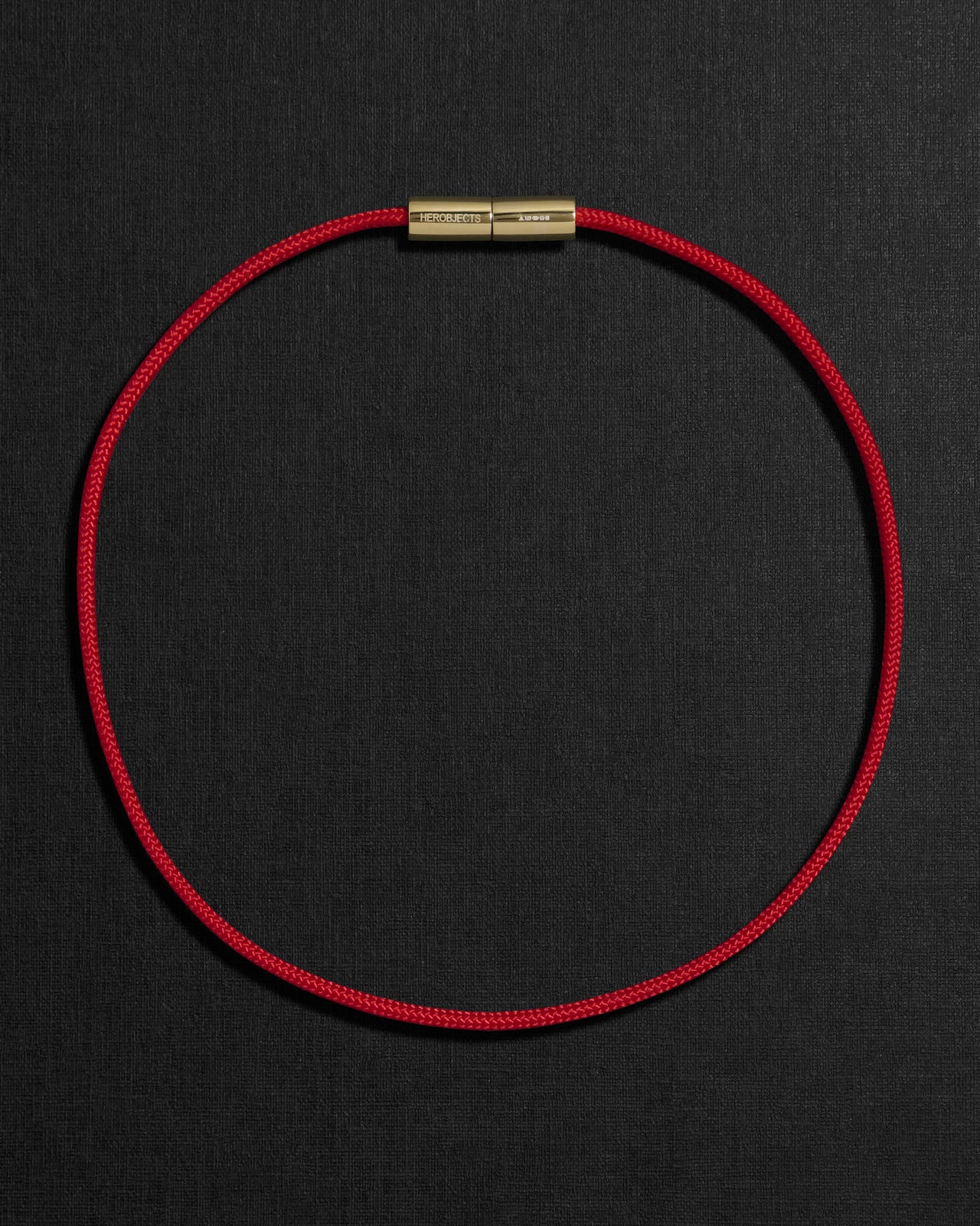 Red cord necklace with a 18K gold clasp on a black background