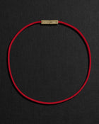 Red cord necklace with a 18K gold clasp on a black background
