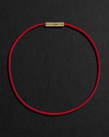 Red cord necklace with a 18K gold clasp on a black background