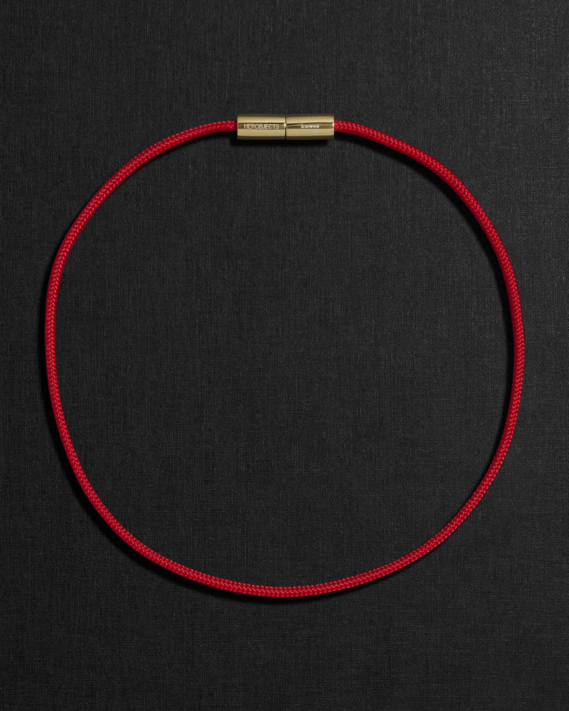 Red cord necklace with a 18K gold clasp on a black background