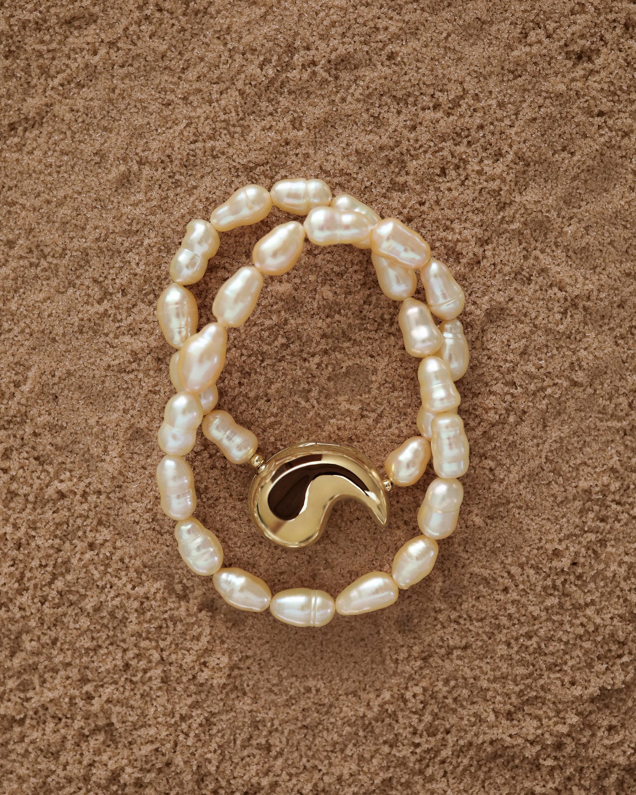 18K Gold Hero Spiral pendant and 18K Gold Peach freshwater pearl on a sand