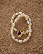 18K Gold Hero Spiral pendant and 18K Gold Peach freshwater pearl on a sand