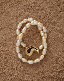 18K Gold Hero Spiral pendant and 18K Gold Peach freshwater pearl on a sand